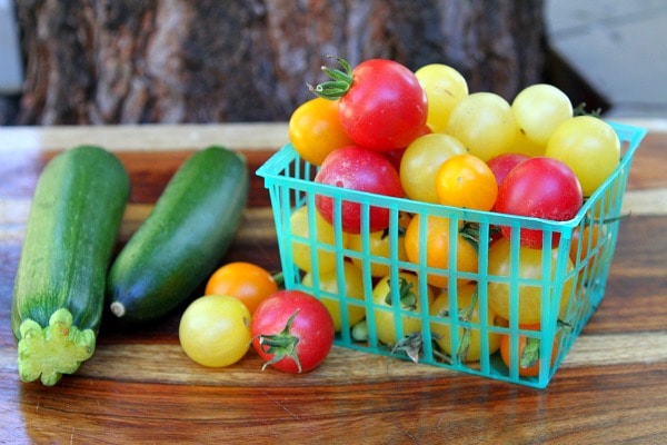 Cherry tomatoes red and yellow in a green plastic basket and two zucchini on a cutting board