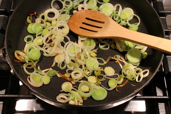 Sauteing Leeks in a skillet on the stove with a wooden spoon