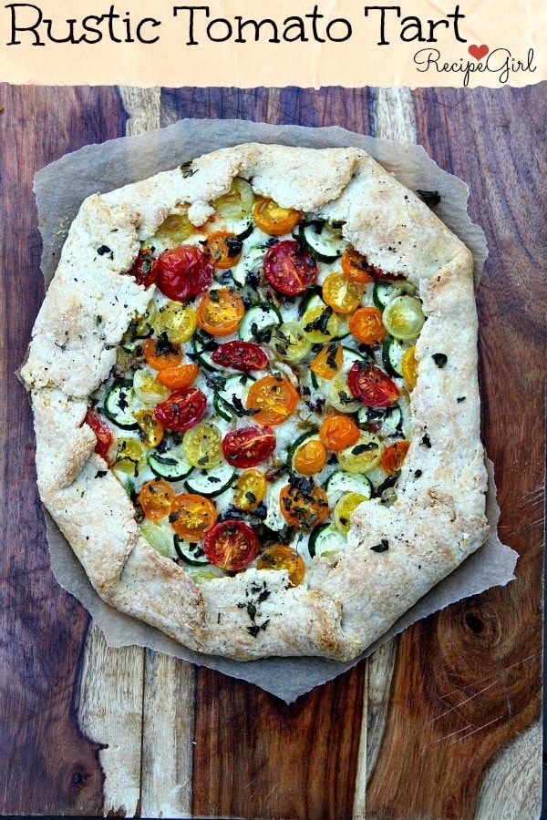 overhead shot of rustic tomato and zucchini tart on parchment paper sitting on a wooden cutting board