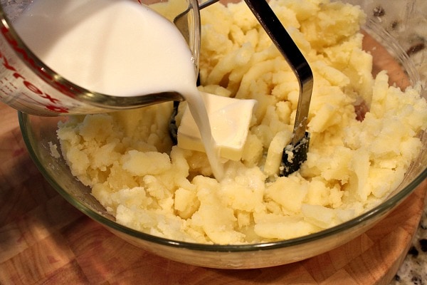 pouring milk and butter onto mashed potatoes in bowl