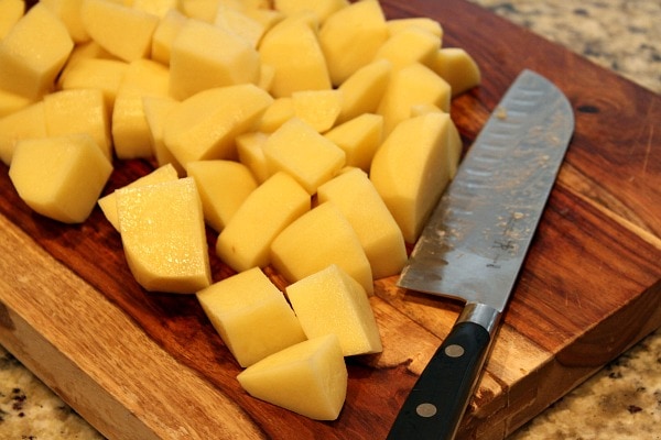 Perfect Mashed Potatoes recipe from RecipeGirl.com #perfect #mashed #potatoes #recipe #RecipeGirl Cutting potatoes on cutting board with knife