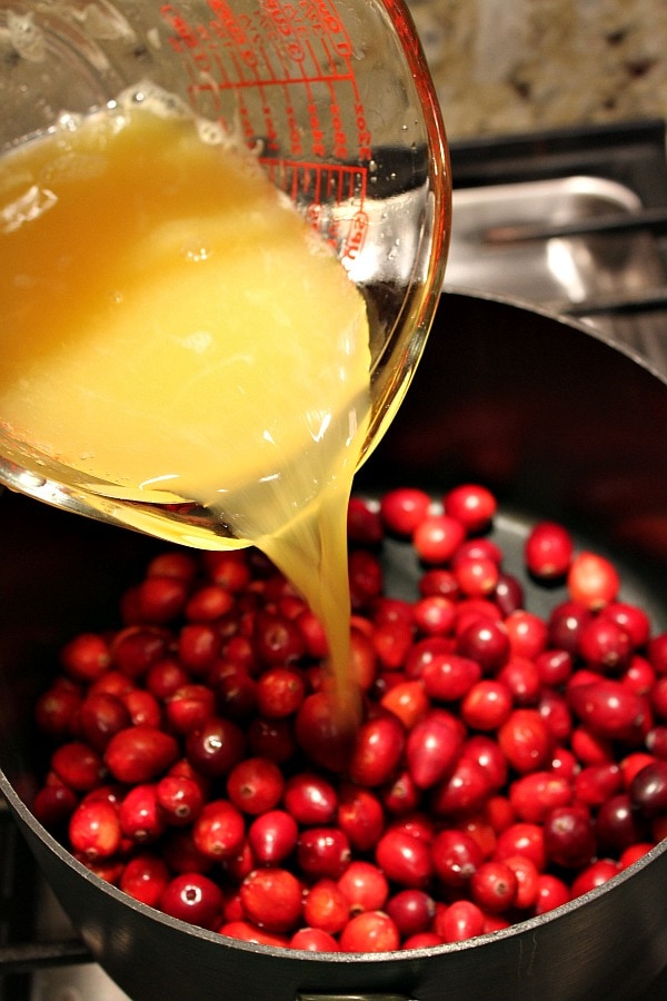 Pouring orange juice into pan with cranberries