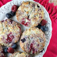 overhead shot of fresh berry scones on a white platter with scattered fresh berries around. pink cloth napkin underneath