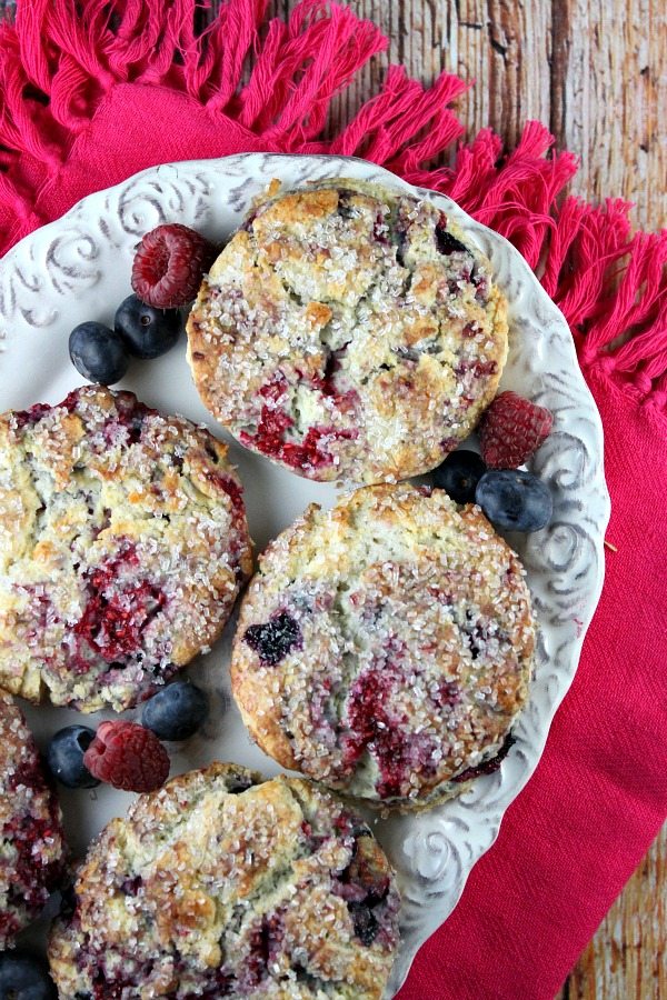 Overhead shot of berry scones on a white serving platter with fresh berries, set on a bright pink cloth napkin on a wooden board