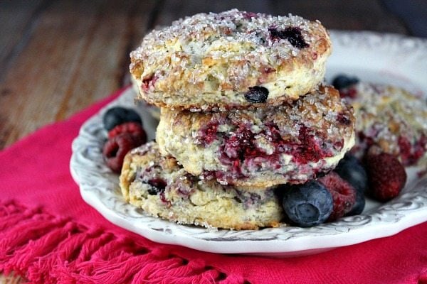 Berry Scones stacked on a white serving platter with fresh berries scattered around. Set on a bright pink cloth napkin.