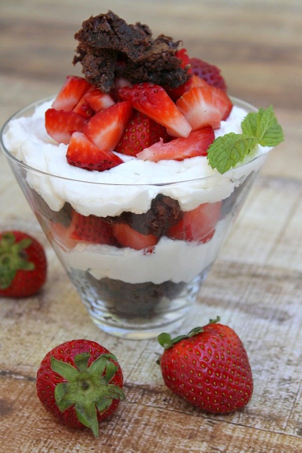 Brownie Strawberry Shortcake in a clear glass with fresh strawberries scattered around
