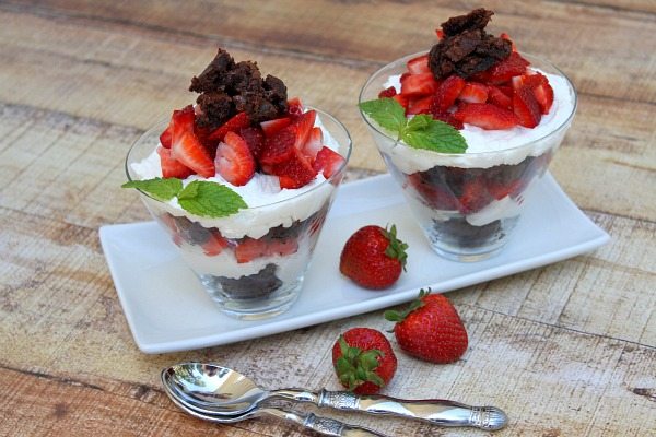 two Brownie Strawberry Shortcakes on a white serving plate with two spoons and strawberries scattered around