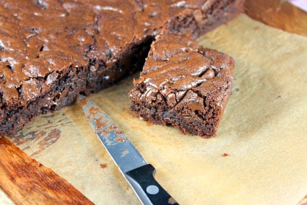 Brownies on a cutting board with a knife and with one piece displayed and the rest in the background