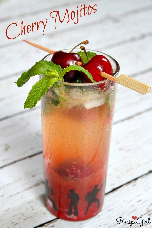 Cherry Mojito garnished with pick of fresh cherries and fresh mint, displayed on a white wood plank board