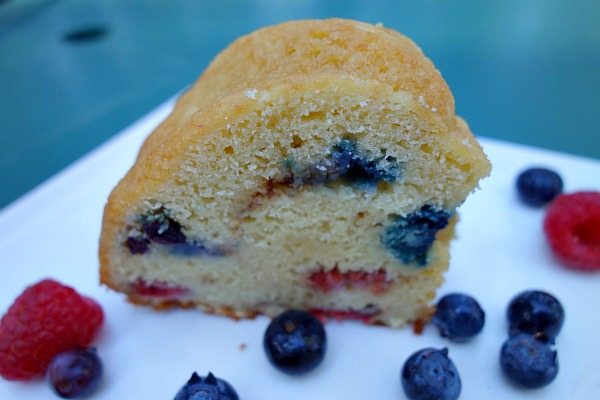 slice of two berry coffee cake with fresh berries scattered around