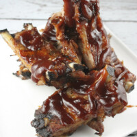 ribs on a white plate drizzled with barbecue sauce