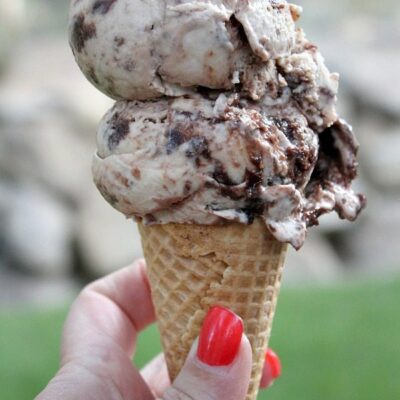 toasted marshmallow brownie malt ice cream scoop on a sugar cone with a hand holding the cone