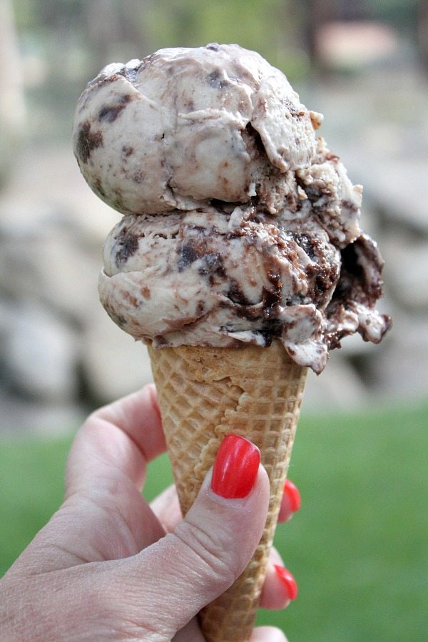 toasted marshmallow brownie malt ice cream scoop on a sugar cone with a hand holding the cone