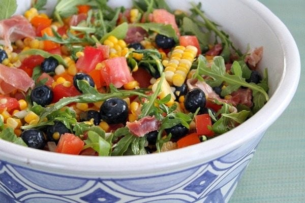 blueberry corn salad with prosciutto in a blue and white ceramic bowl