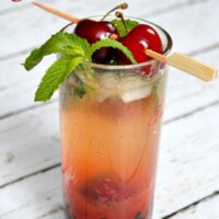 cherry mojito displayed on a white wood plank surface garnished with fresh cherries and mint