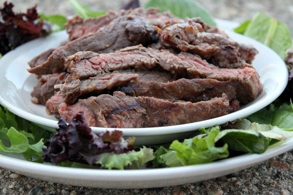 Marinated, Grilled Skirt Steak cut into slices and displayed on a white platter surrounded by lettuce leaves