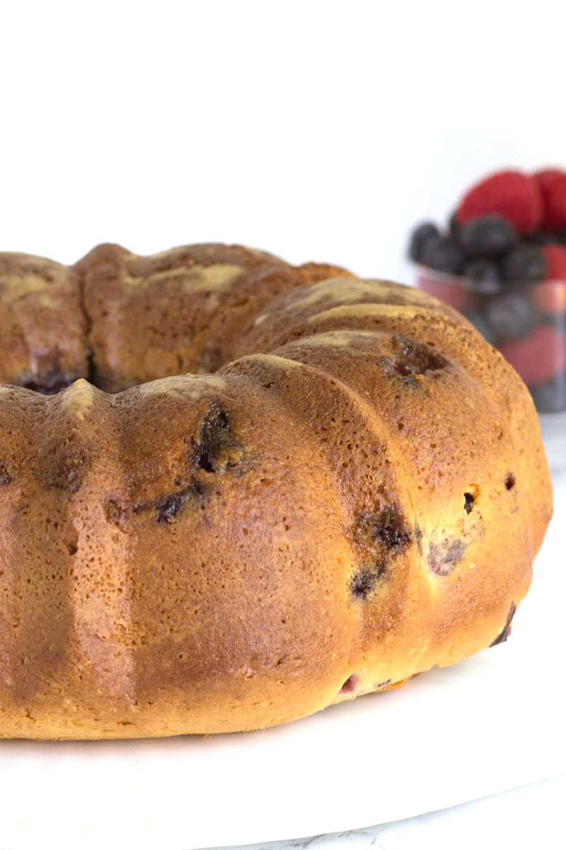 two berry coffee cake on a white platter with a bowl of berries in the background