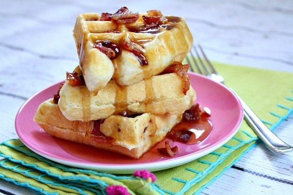 three waffles stacked with maple syrup and bacon