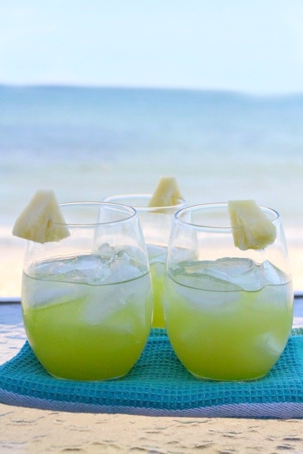 two pearl harbor cocktails sitting side by side garnished with pineapple sitting on a blue towel with the ocean in the background