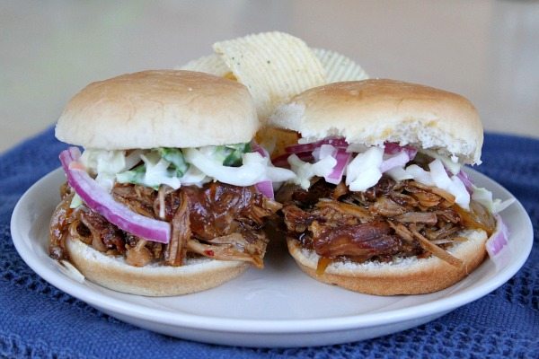 Two Slow Cooker Pulled Pork Sliders on a white plate with chips, set on a blue tablecloth