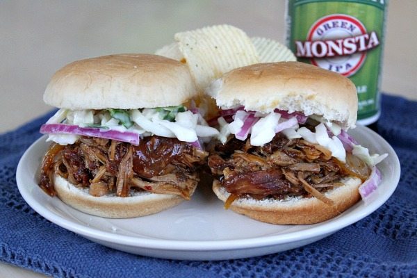 Two Slow Cooker Pulled Pork sliders on a white plate with potato chips and a can of green monsta beer, set on a blue napkin