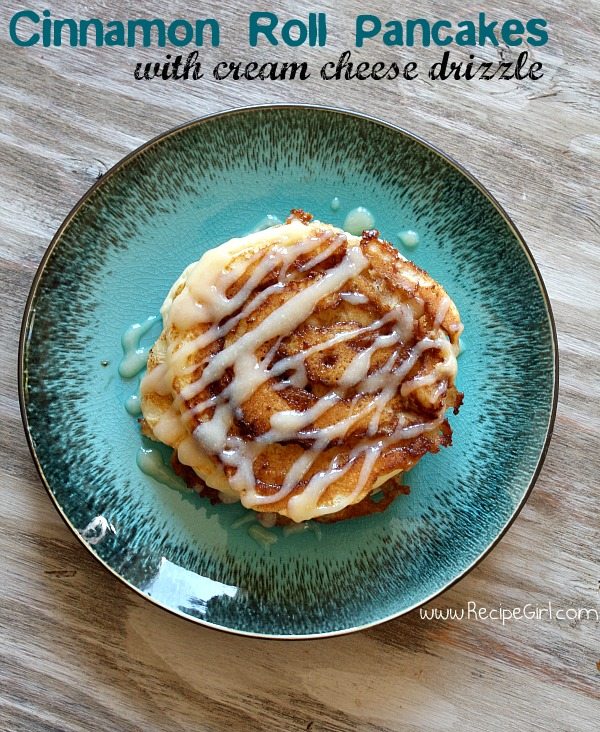 overhead shot of cinnamon roll pancakes with cream cheese drizzle on a teal green plate on a wooden board