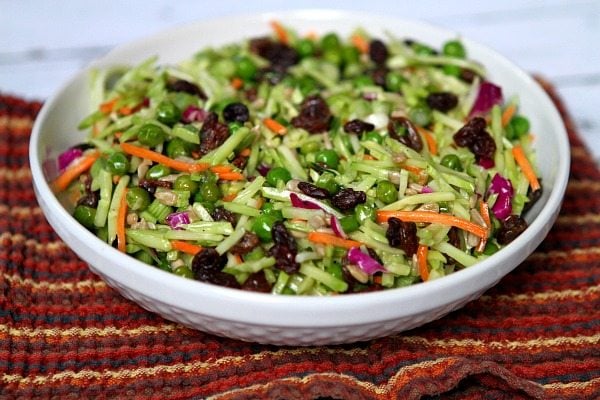 broccoli slaw in a white serving bowl set on top of a striped burgundy cloth napkin