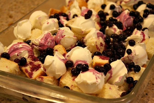 preparing overnight blueberry french toast in a glass casserole dish with bread, cream cheese and blueberries