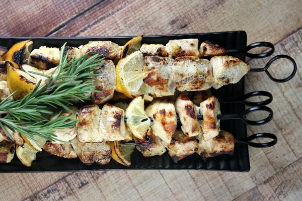 Rosemary lemon chicken skewers on a black tray with fresh lemon and fresh rosemary garnish