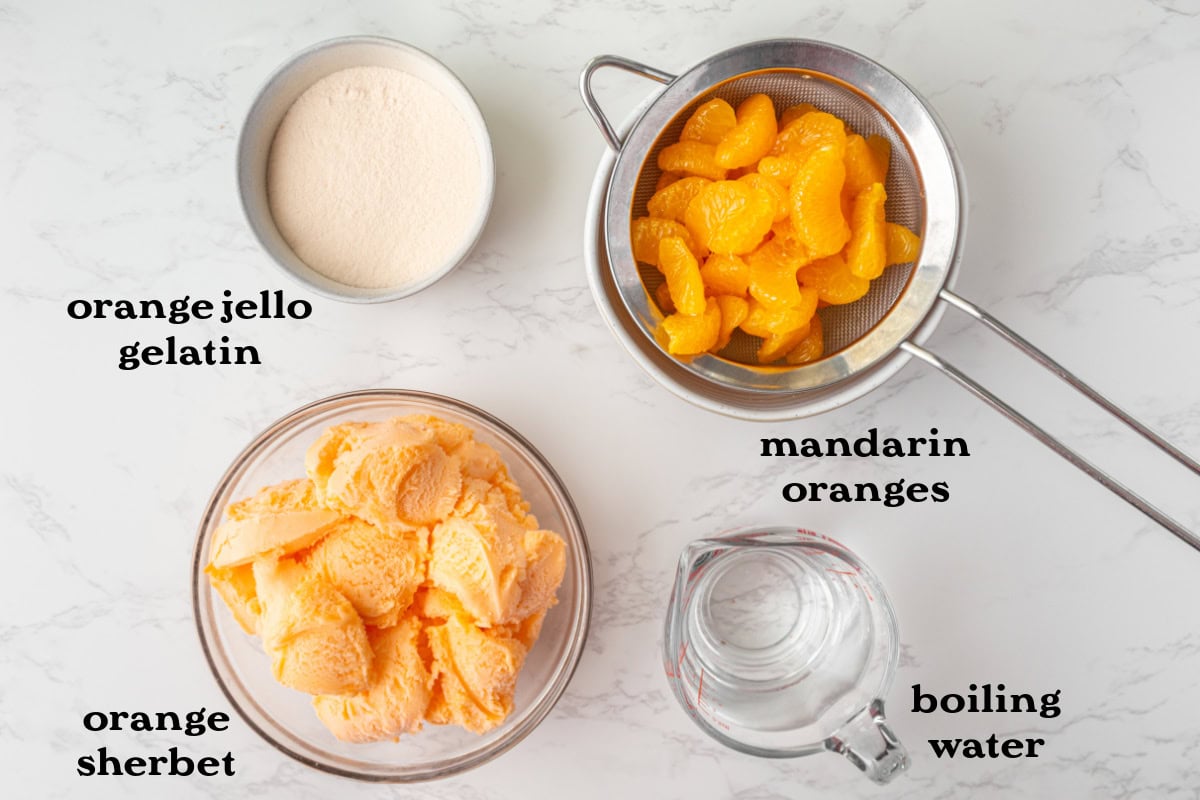 Cool, creamy, and perfectly nostalgic — this Orange Sherbet Jello Salad is made with orange Jell-O, sherbet, and mandarin oranges. The perfect citrusy dessert for holidays, brunches, and family gatherings! four ingredients displayed to make orange sherbet jello salad