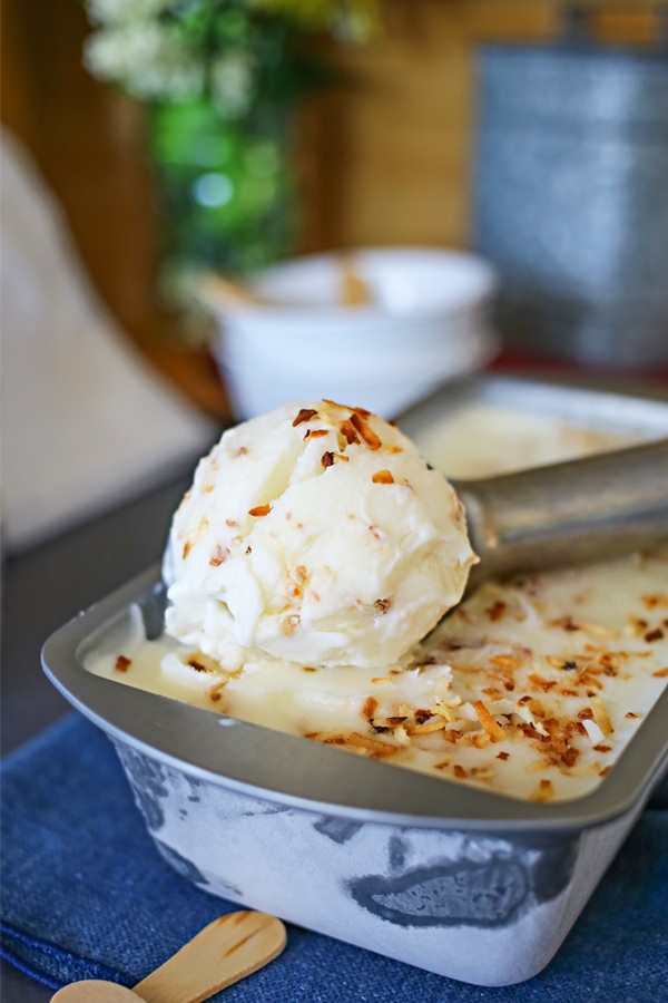 Coconut Frozen Yogurt being scooped out of a tin with an ice cream scoop sitting on a blue tablecloth