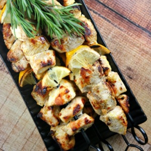 Rosemary lemon chicken skewers on a black tray with fresh lemon and fresh rosemary garnish