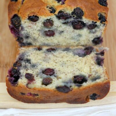 loaf of banana blueberry bread sliced open to see the inside on a cutting board