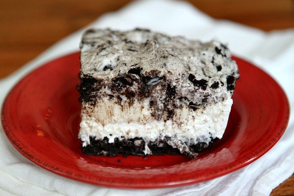 slice of no bake oreo cheesecake bar on a red plate on top of a striped white cloth napkin
