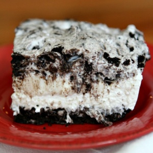 slice of no bake oreo cheesecake bar on a red plate on top of a striped white cloth napkin