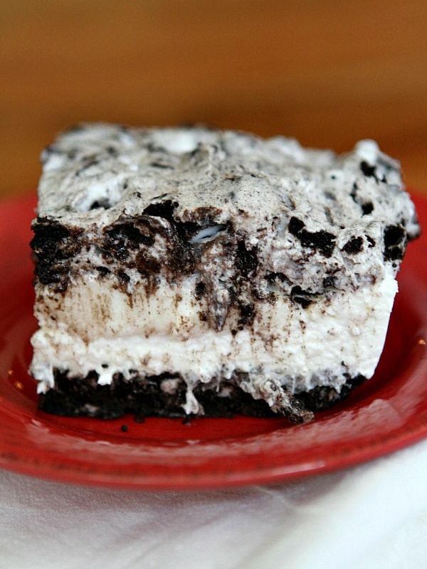 slice of no bake oreo cheesecake bar on a red plate on top of a striped white cloth napkin