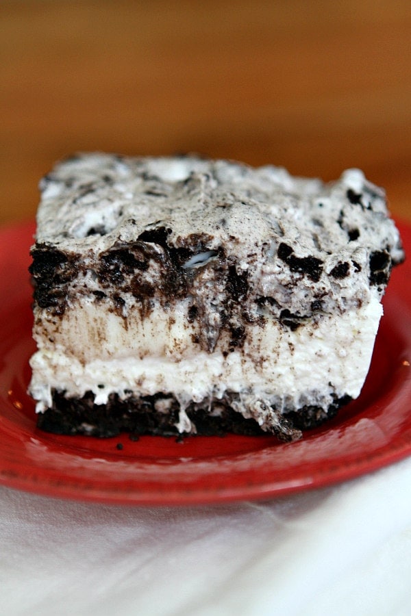 slice of no bake oreo cheesecake bar on a red plate on top of a striped white cloth napkin