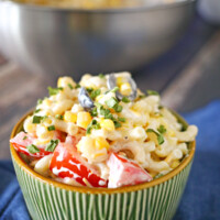 Summer Macaroni Salad in a green bowl sitting on a blue cloth napkin with a stainless steel bowl in the background