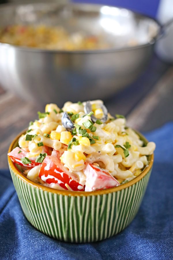 Summer Macaroni Salad in a green bowl sitting on a blue cloth napkin with a stainless steel bowl in the background