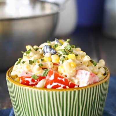Summer Macaroni Salad in a green bowl sitting on a blue cloth napkin with a stainless steel bowl in the background