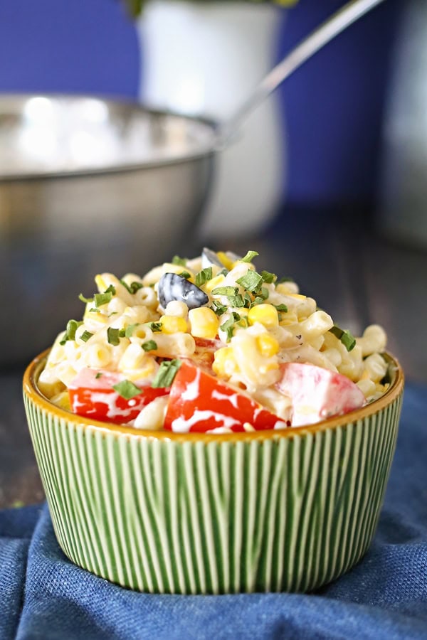 Summer Macaroni Salad in a green bowl sitting on a blue cloth napkin with a stainless steel bowl in the background