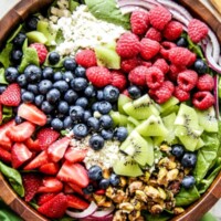 Overhead shot of kiwi berry salad in a wooden salad bowl with a green cloth napkin on the side