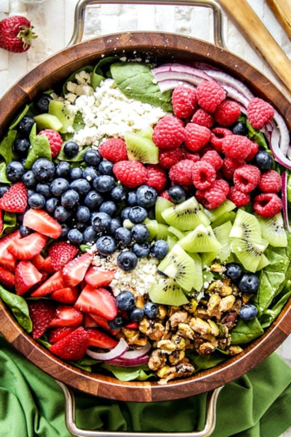 Overhead shot of kiwi berry salad in a wooden salad bowl with a green cloth napkin on the side