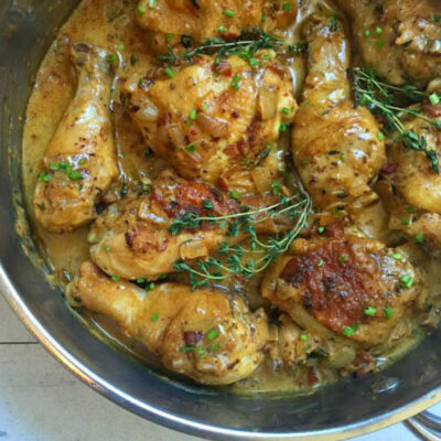 chicken pieces cooking in pan with sauce and fresh thyme