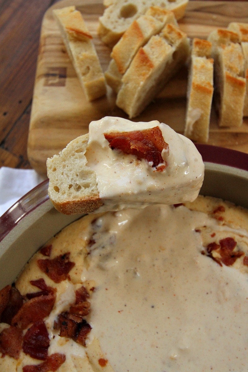 Baguette dipped in Beer and Bacon Dip with sliced baguette in the background