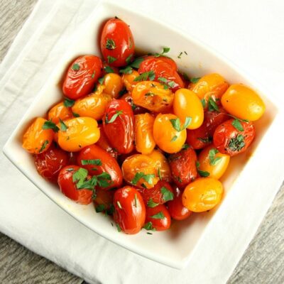 overhead shot of sauteed tomatoes with thyme in a white bowl garnished with fresh parsley sitting on a white cloth napkin