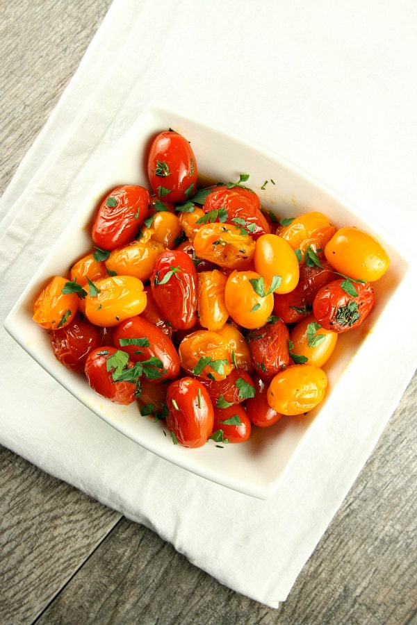 overhead shot of sauteed tomatoes with thyme in a white bowl garnished with fresh parsley sitting on a white cloth napkin