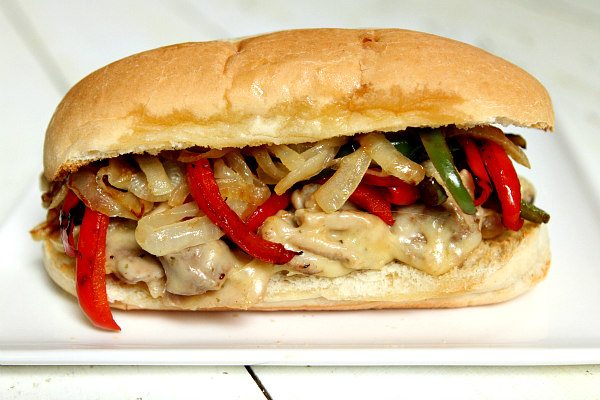pork and melted cheese hoagie with added bell peppers and onions on a white plate