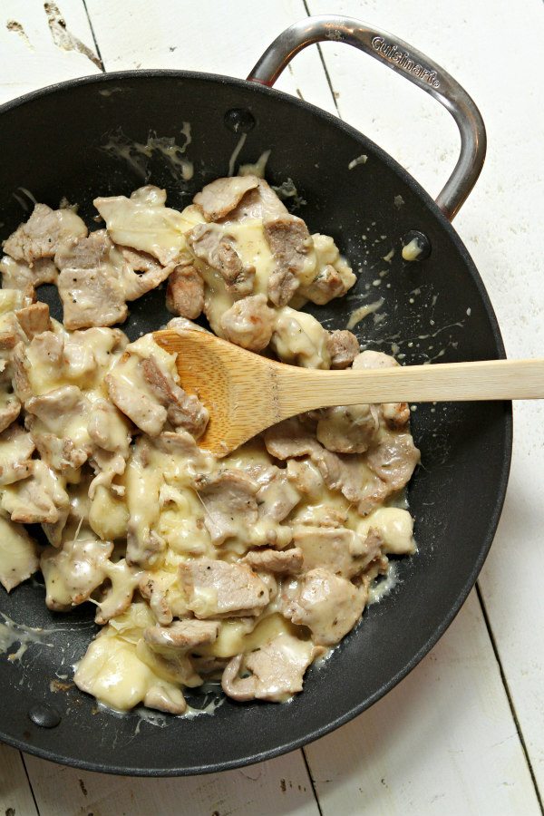 pork and melted cheese being cooked in a skillet with a wooden spoon