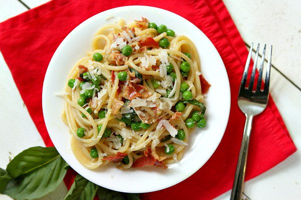 overhead shot of Spaghetti Carbonara on a white plate set on a red napkin with a fork and fresh basil leaves on the side